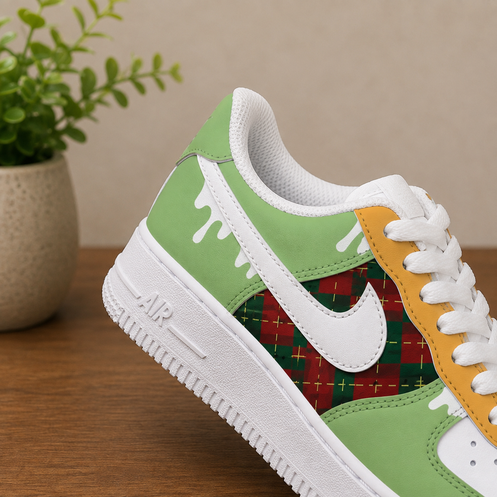 A close-up of a green and white sneaker with a red and green plaid pattern panel, white dripping paint details, and yellow eyelets, resting on a wooden surface with a potted plant in the background.