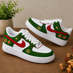 A pair of white Nike Air Force 1 style sneakers decorated with a Christmas theme, featuring green panels, a red Swoosh, gold snowflakes, and red-and-green ornament details, displayed on a wooden surface.