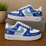 A pair of customized Nike Air Force 1 style sneakers in blue and white, decorated with stars, a globe graphic, and text reading 'Midnight's' and '(Taylor's version)' / '(3am edition)'. The shoes are displayed on a wooden table with a gray shoebox and a potted plant in the background.