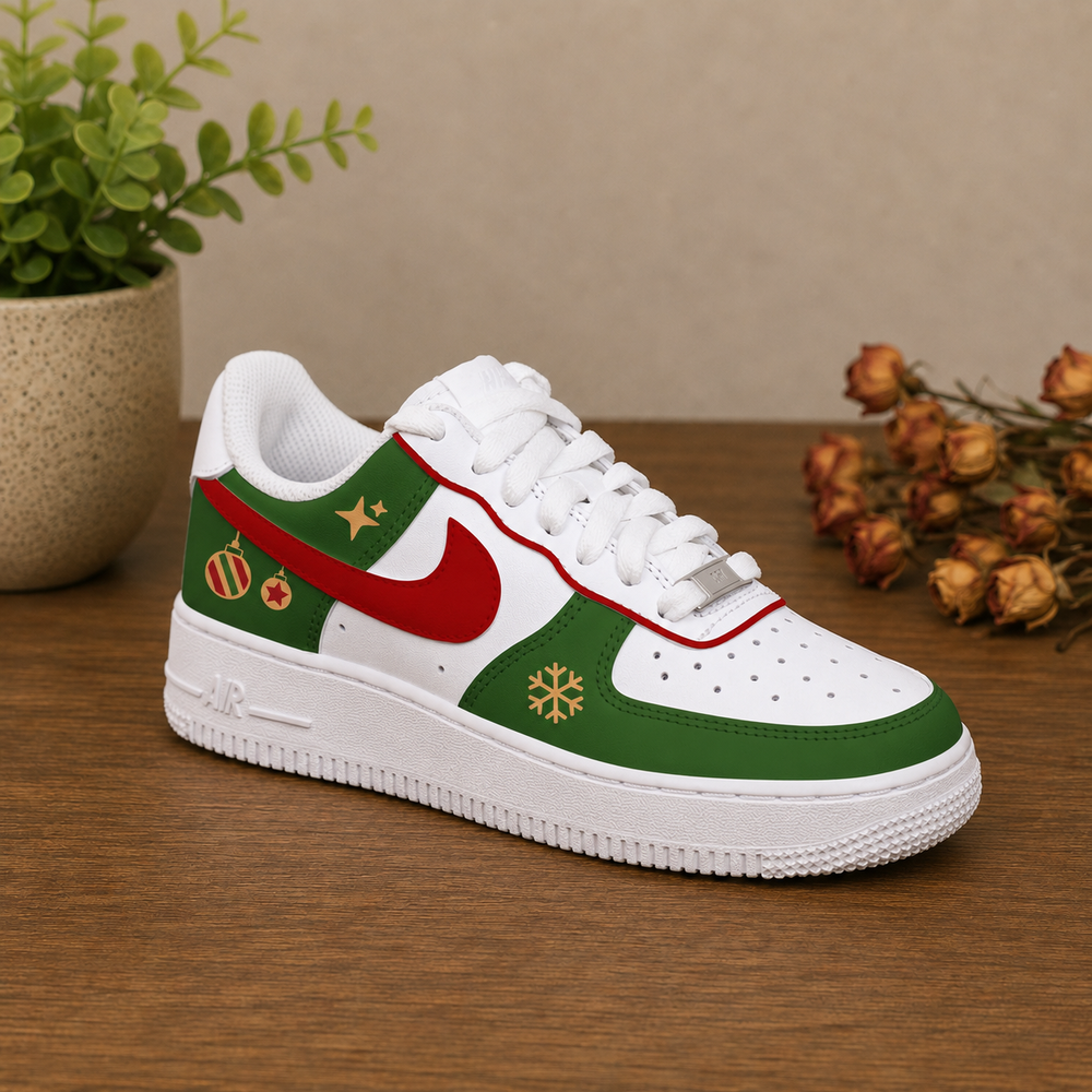 A single low-top sneaker styled with a Christmas theme, featuring a white base with green panels, a red swoosh, gold snowflake and ornament details, and a white sole, displayed on a wooden table with a potted plant and dried flowers in the background.