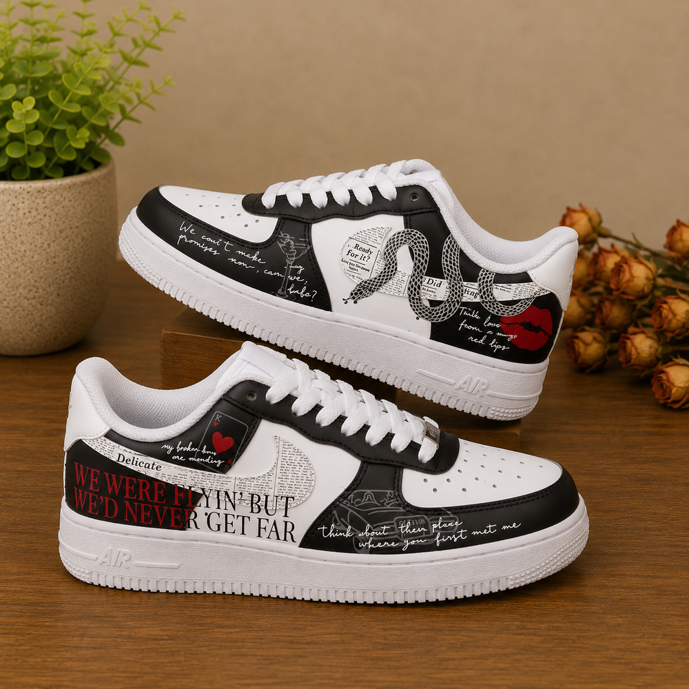 A pair of custom white and black low-top sneakers with graphic prints, displayed on a wooden surface with decorative plants and dried flowers in the background.