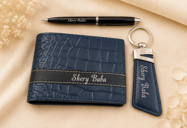Personalized navy blue faux-crocodile leather wallet and matching keychain set with a black pen, all engraved with 'Shery Baba' on a beige fabric background with dried flowers.