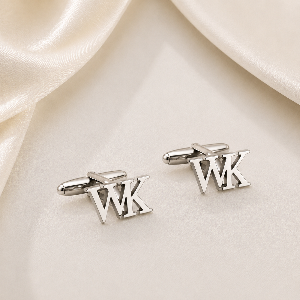 A pair of silver initial cufflinks spelling 'WK', displayed on a cream satin fabric background.