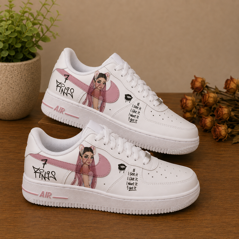 A pair of white Air Force 1 style sneakers with custom illustrations and text, displayed on a wooden surface with a potted plant and dried flowers in the background.