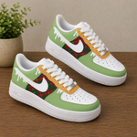 A pair of Nike Air Force 1 style sneakers with a holiday-themed design, featuring light green panels, white overlays, a red and green tartan plaid pattern, and yellow paint-drip details, displayed on a wooden surface.