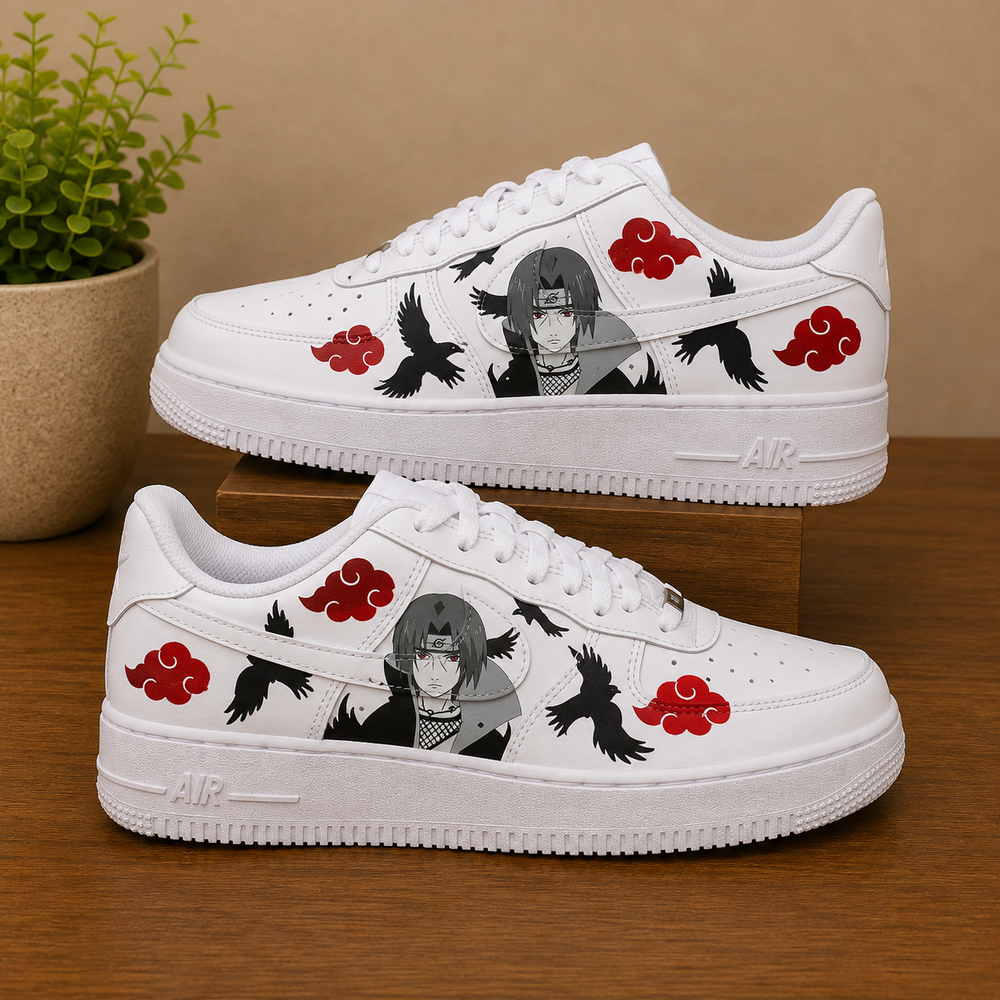 A pair of white low-top sneakers with custom Naruto character graphics, red cloud motifs, and black crows, displayed on a wooden surface with a potted plant in the background.