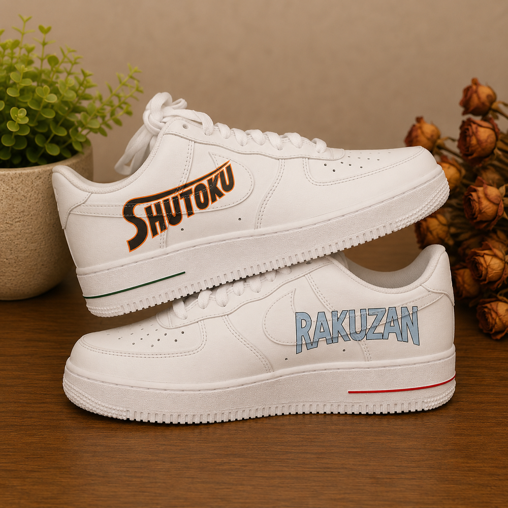 A pair of white low-top sneakers displayed on a wooden surface. The top shoe is positioned above the bottom shoe, with the top shoe's heel side showing the word 'SHUTOKU' in orange and black, and the bottom shoe's side panel showing 'RAKUZAN' in light blue.