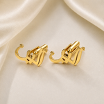 A pair of gold-toned clip-on hoop earrings with a sculptural, abstract curved design, displayed on a draped cream satin fabric background.